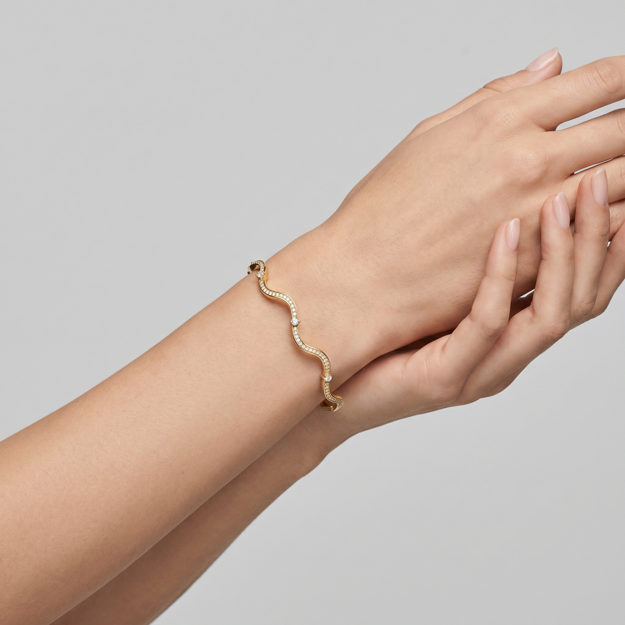 Gold bracelet on a wrist with a neutral background